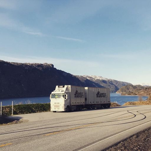 En av Nordvest transport sine hvite trailere som er parkert på en lomme ved siden av en vei med fjell og fjord i bakgrunnen