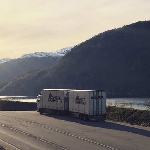 En av Nordvest transport sine hvite trailere som er parkert på en lomme ved siden av en vei med fjell og fjord i bakgrunnen